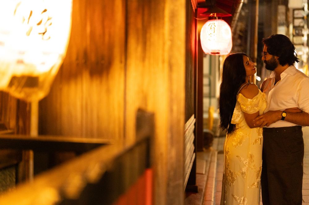 Couple sharing an intimate moment beside a glowing red lantern on a warm evening street.