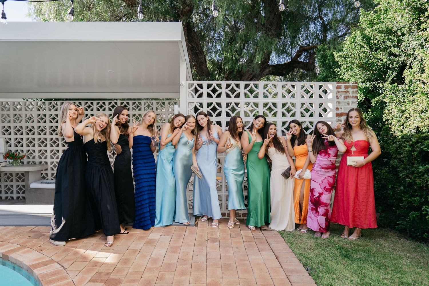 Large group photo of wedding party members in colorful dresses on an outdoor patio.