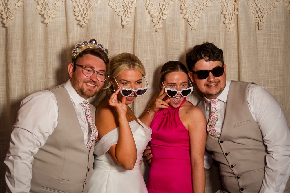 Group of wedding guests having fun with props in a photo booth against beige backdrop.