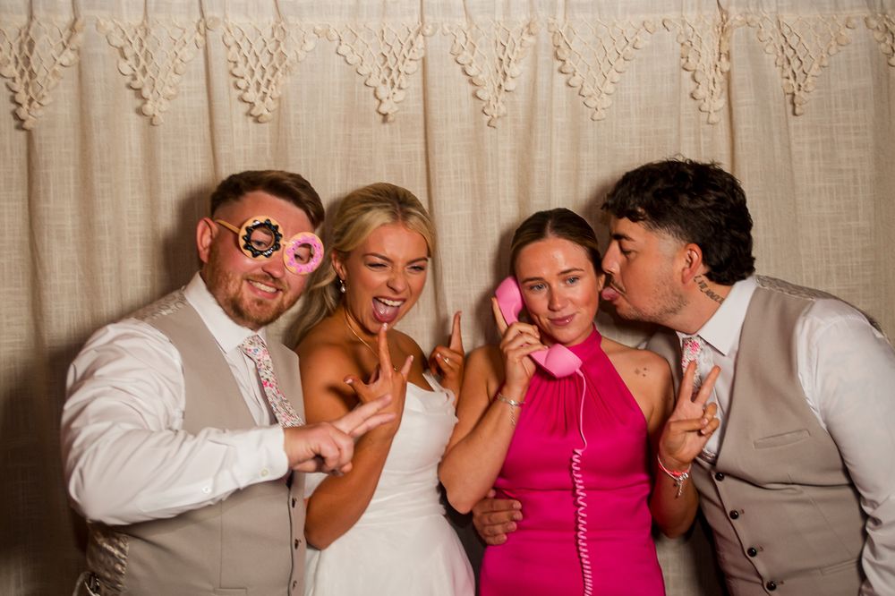Wedding guests pose playfully together in a photo booth with fun props and expressions.