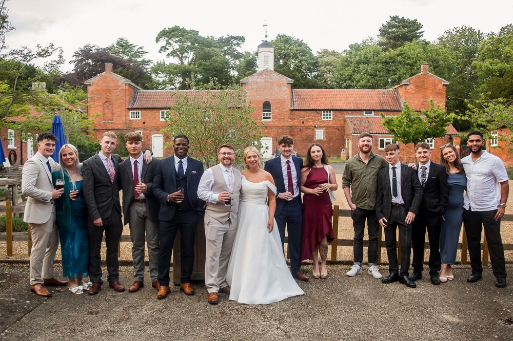 Large group wedding photo with guests lined up outside historic brick building.