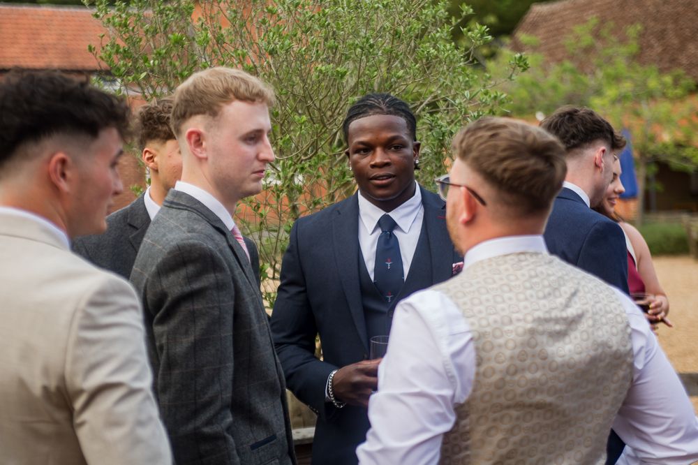Wedding guests gathered outdoors near flowering garden and brick building.