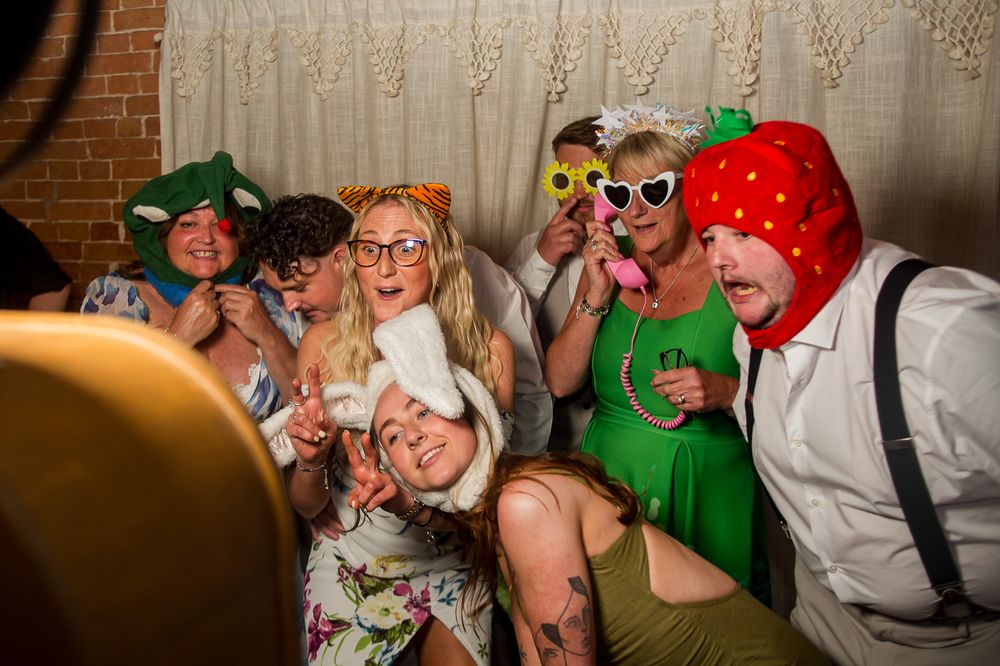 Wedding guests pose with silly props and costumes against a neutral backdrop.