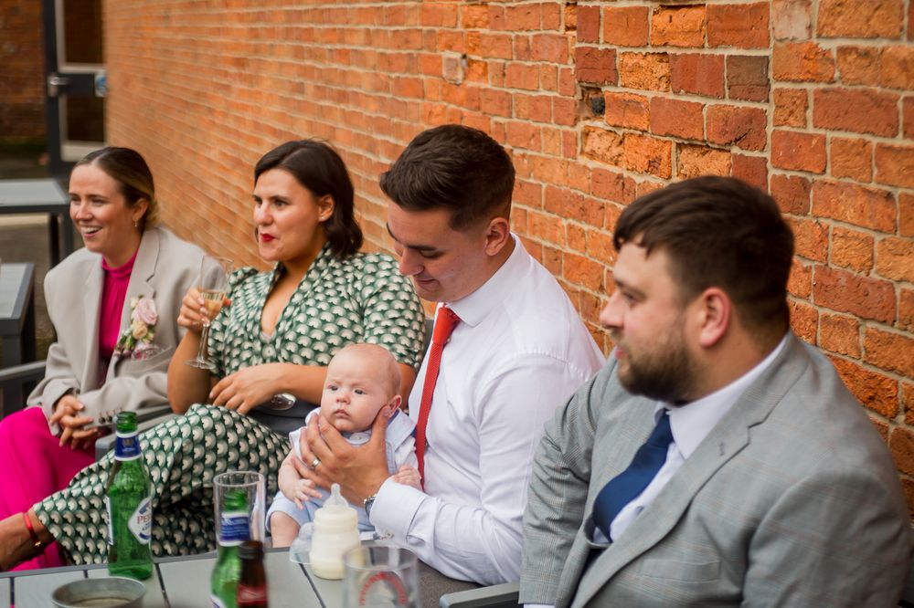 Wedding guests socializing at outdoor reception near brick building.
