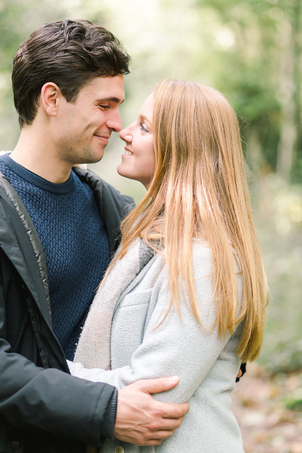 A romantic couple in navy and gray sweaters share tender moments together in a natural outdoor setting.