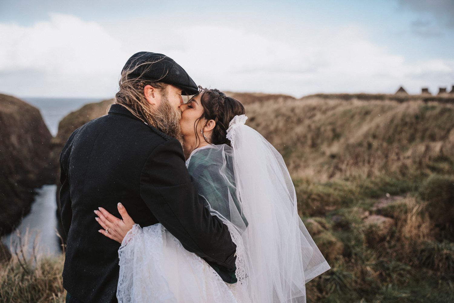 A romantic couple embraces in a dramatic outdoor setting with moody clouds and rolling hills in the background.