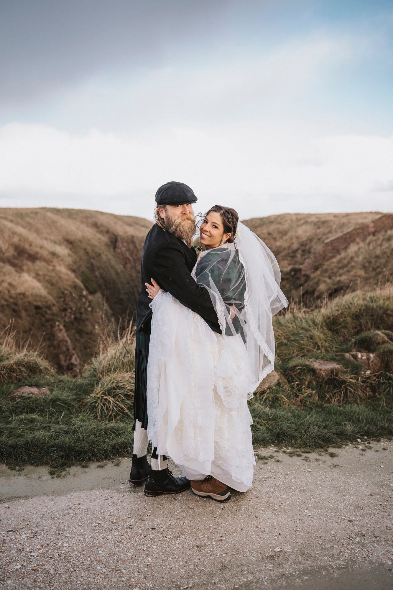 A romantic wedding couple shares intimate moments against a scenic coastal backdrop with rolling hills.