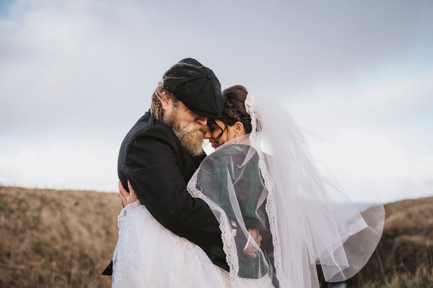 A couple embraces under a flowing white veil against a scenic outdoor landscape during a romantic photoshoot.