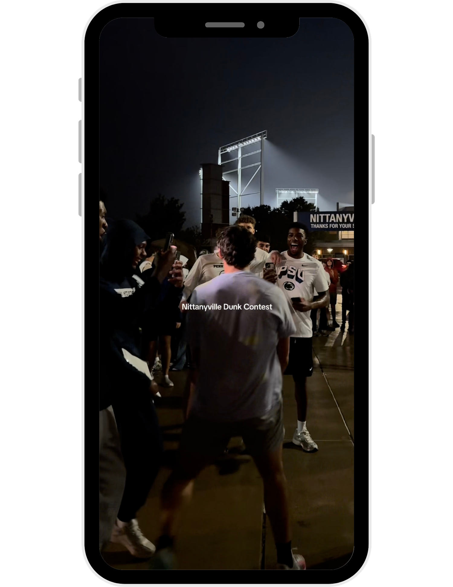 Dark silhouettes of people dancing and socializing at a nighttime outdoor gathering with a lit structure in the background.