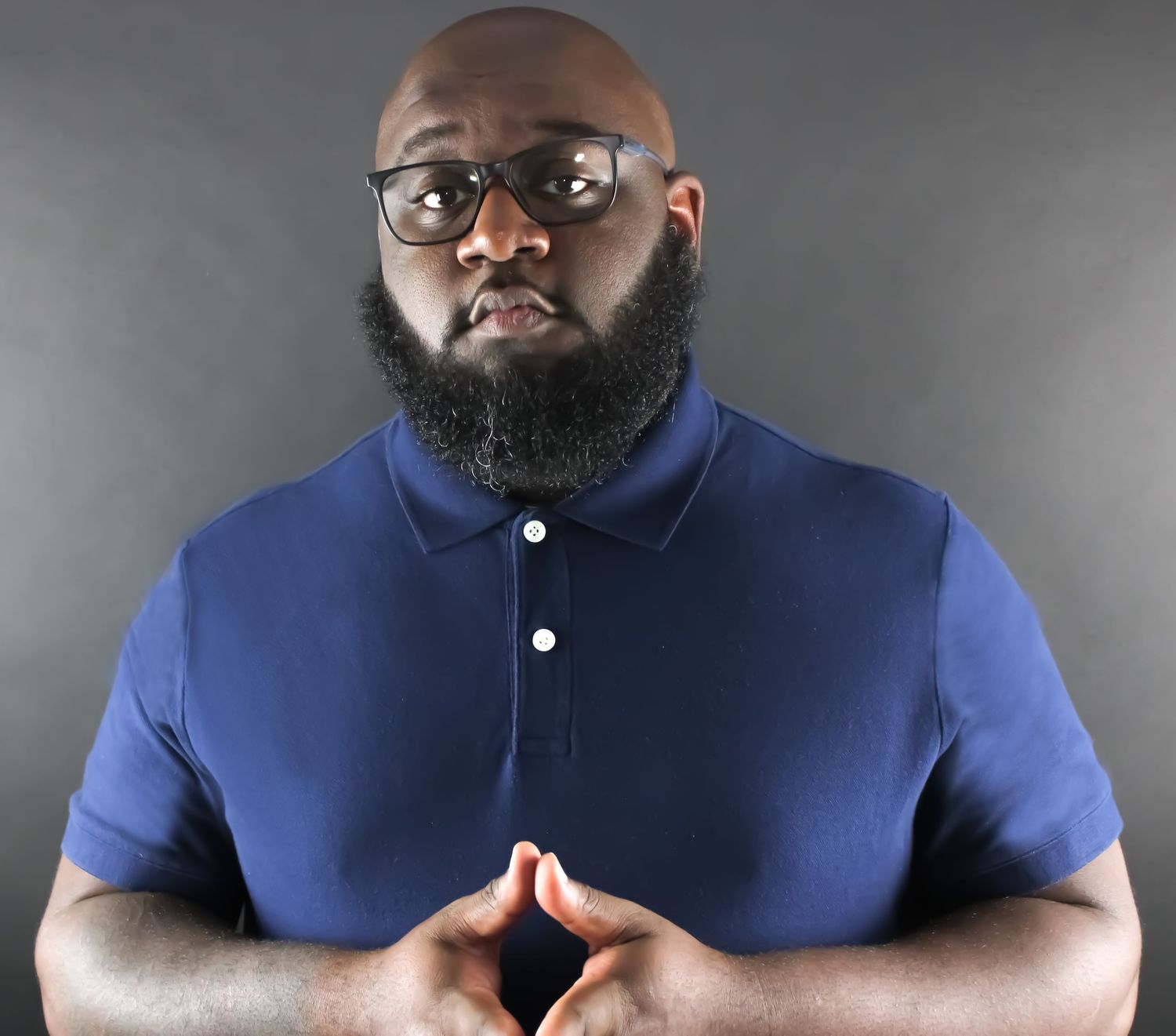 Professional studio portrait of person wearing a navy blue polo shirt and glasses against a gray background.