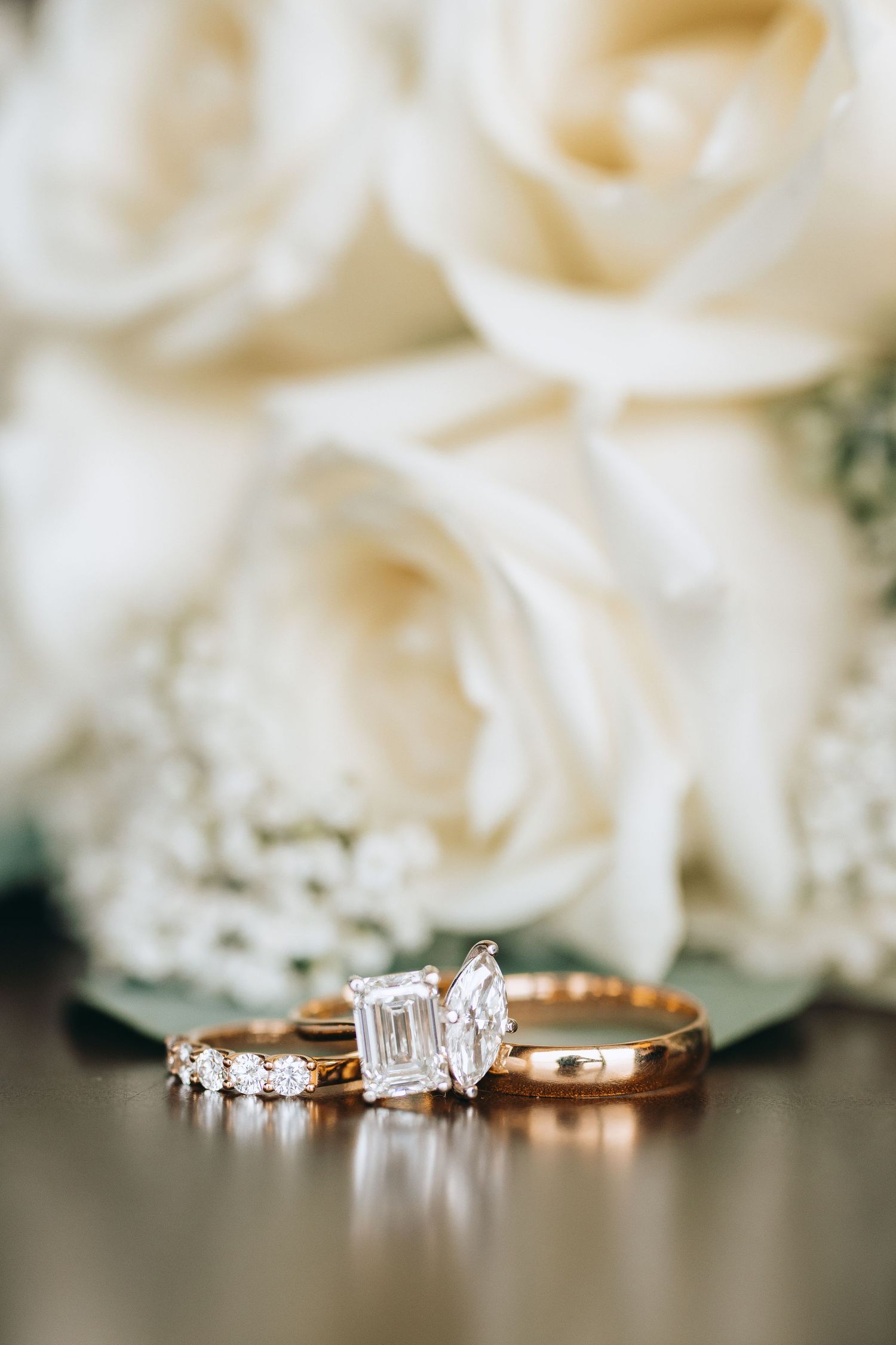 Three wedding rings including diamond engagement ring displayed against soft white roses.
