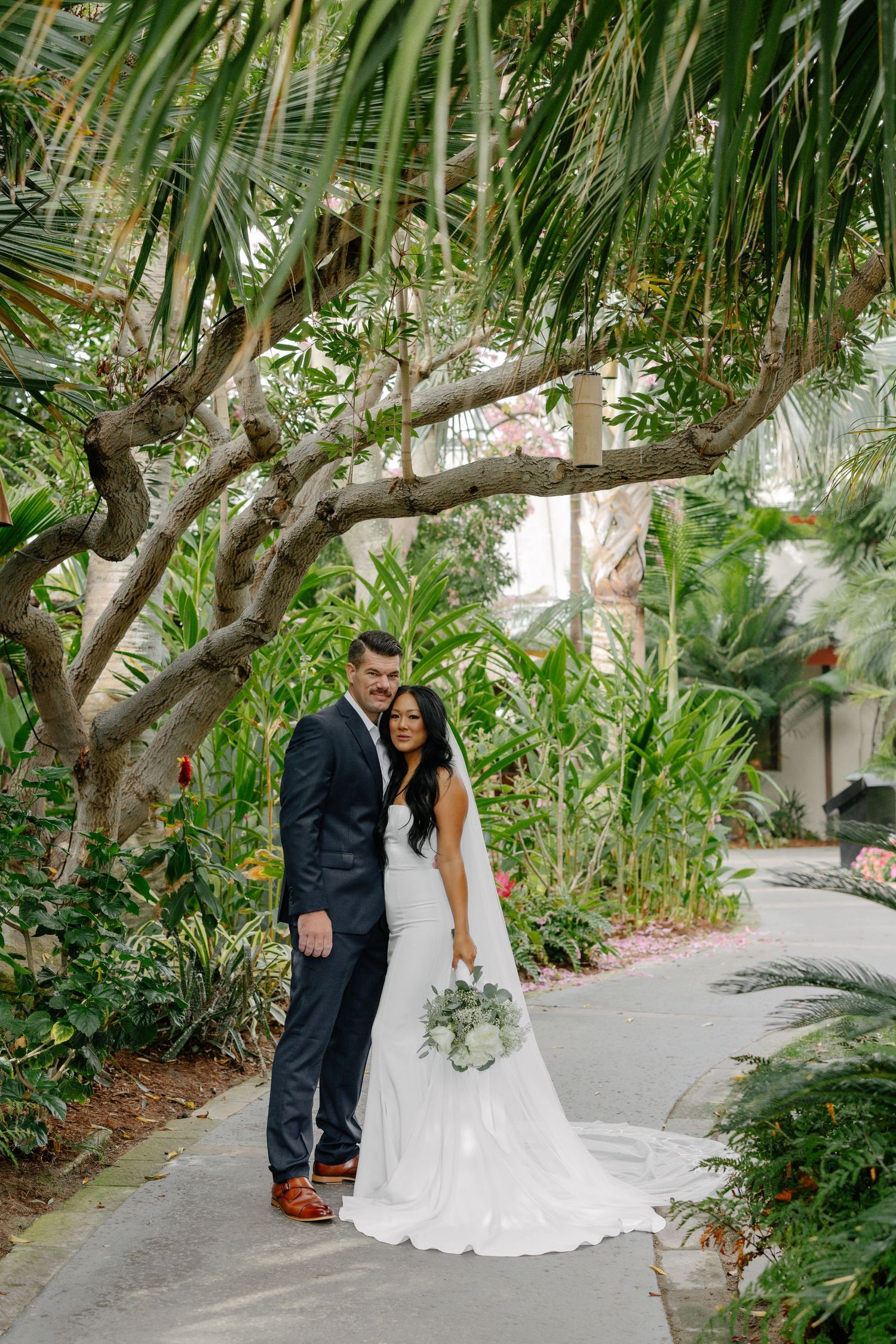 Wedding couple standing beneath palm trees on tropical garden path.