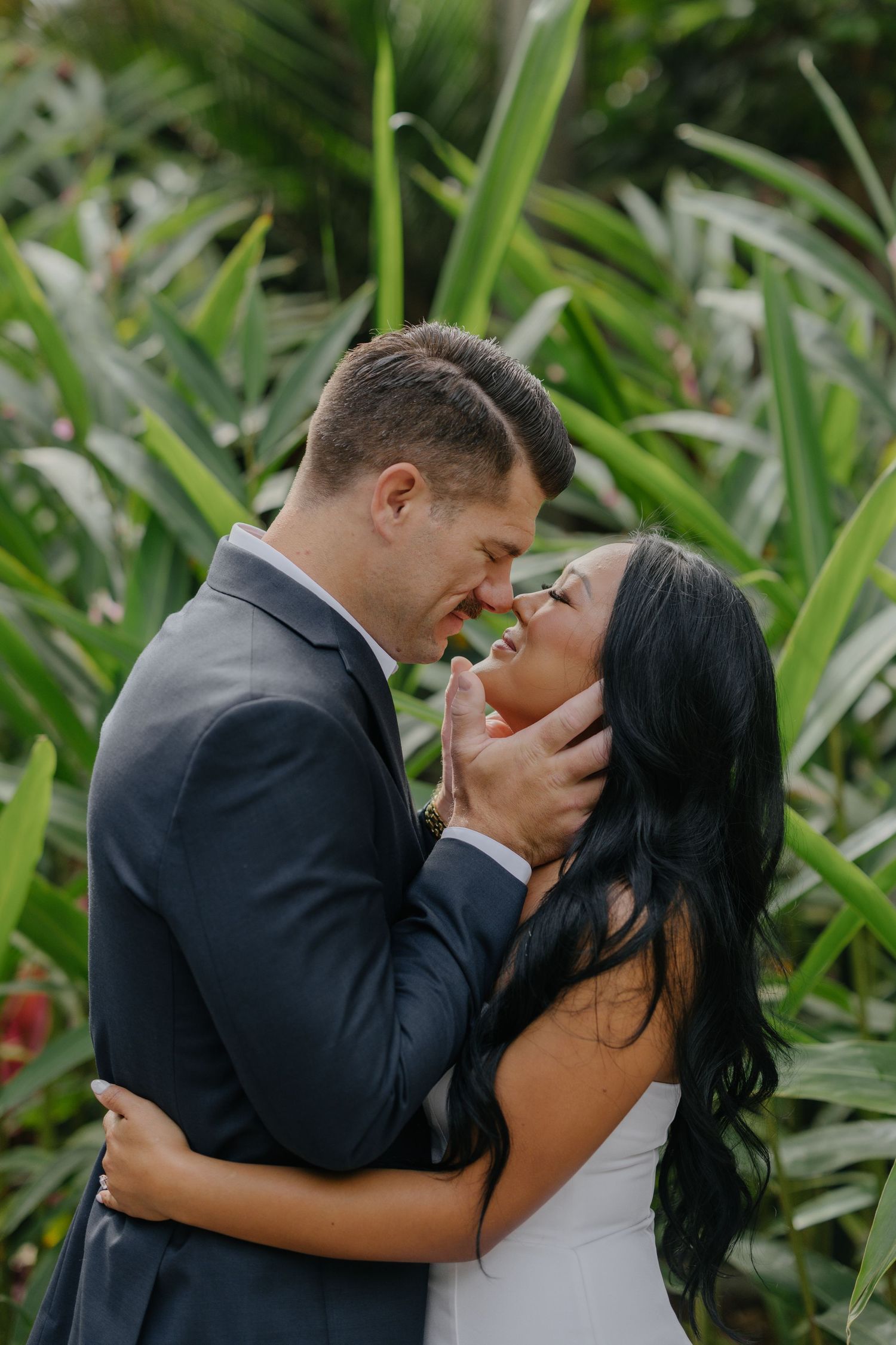 A couple shares an intimate moment against a backdrop of tropical greenery.