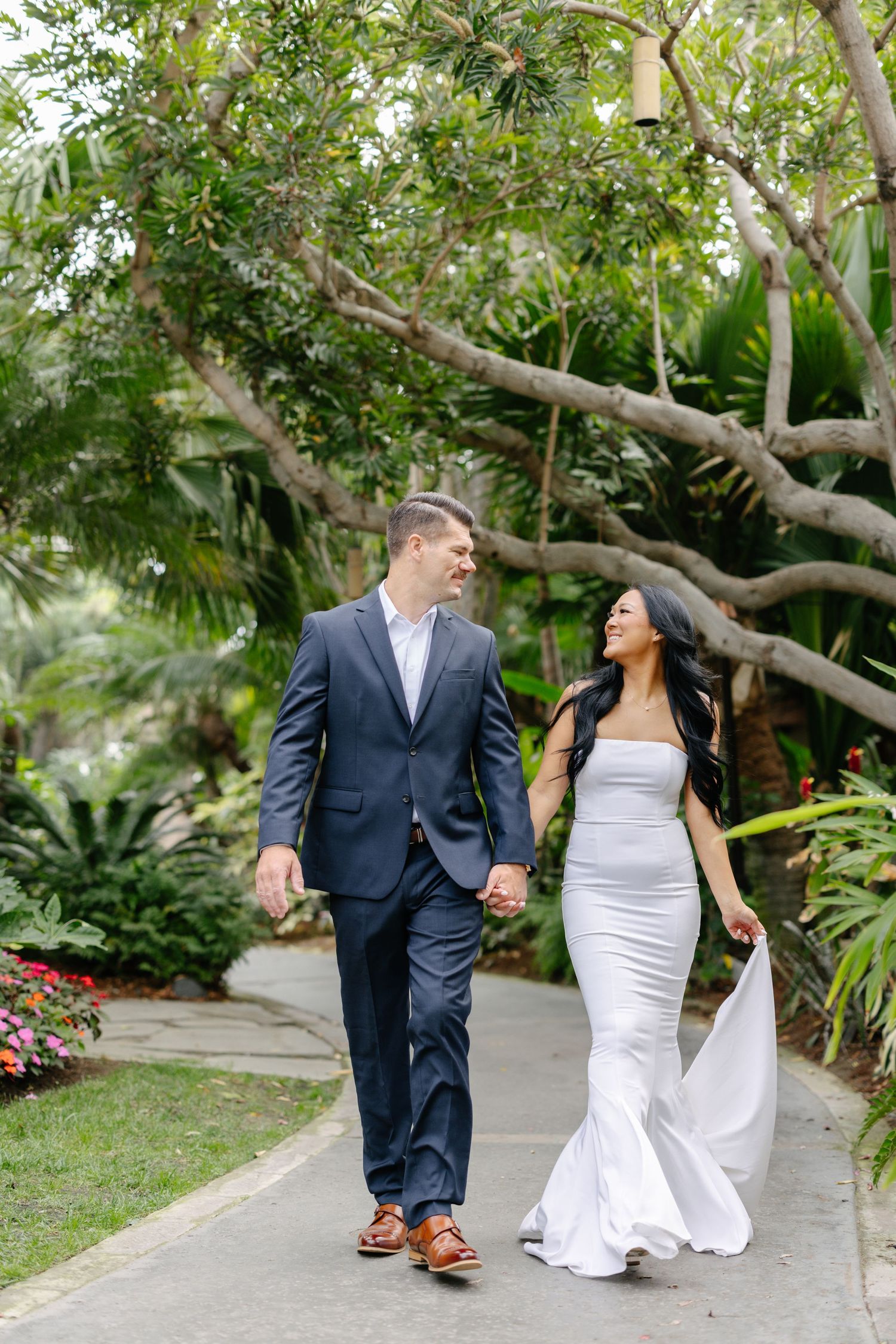 A couple strolls along a garden path surrounded by tropical plants and flowers.