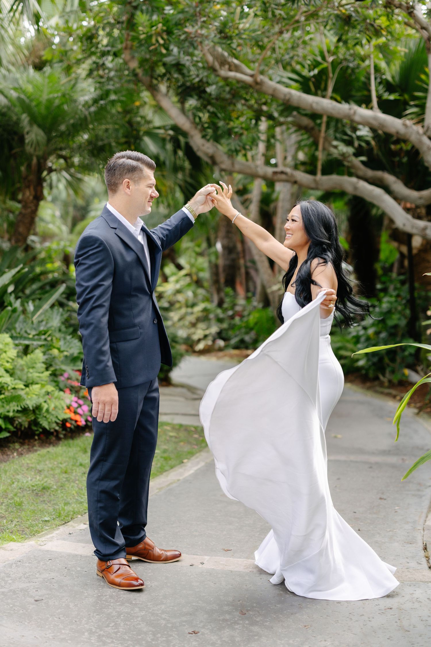 A couple dances playfully on a garden path surrounded by lush greenery.