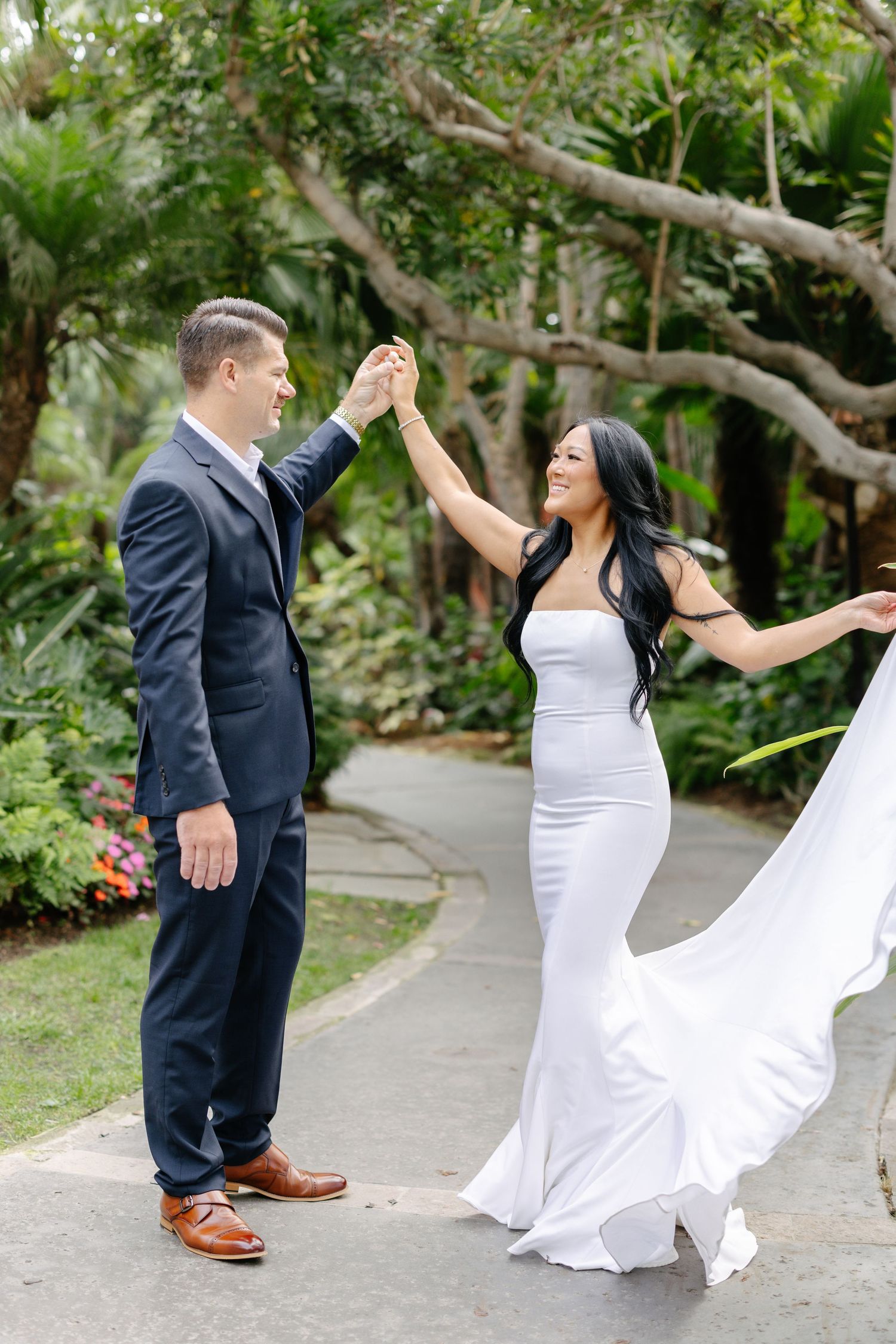 A couple performs a twirling dance move on a garden pathway.