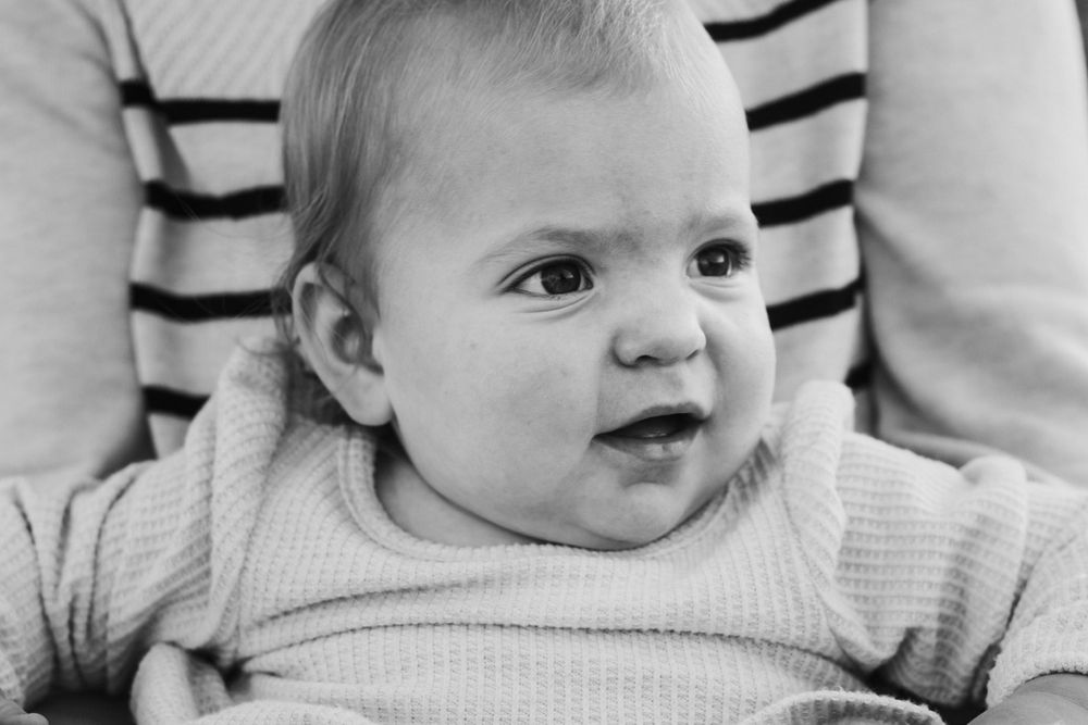 A black and white portrait of an adorable baby with wide eyes and a curious expression.