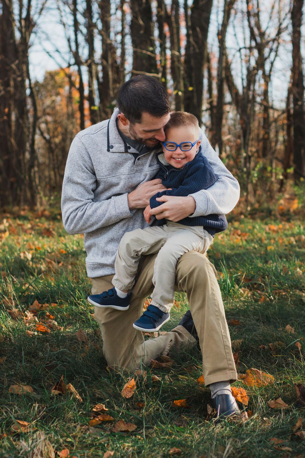 Father kneeling and hugging his young son wearing glasses in autumn park.