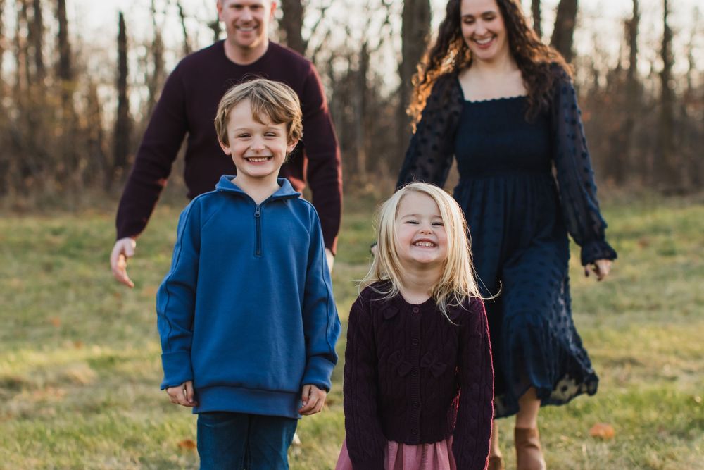 A happy family of four walks together in an open field during autumn.