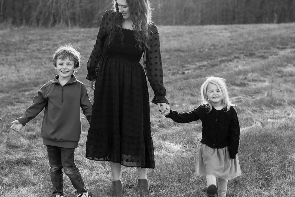 A black and white photo of a mother walking hand-in-hand with her two children in a field.