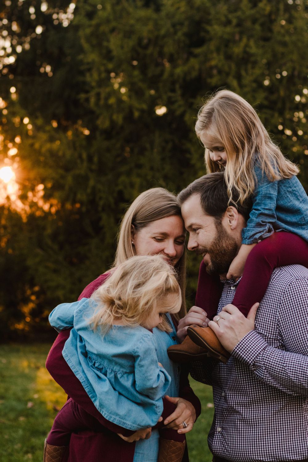 Family smiling with daughter on Father's shoulders during golden hour - lifestyle family photographer in South Lyon, Michigan.
