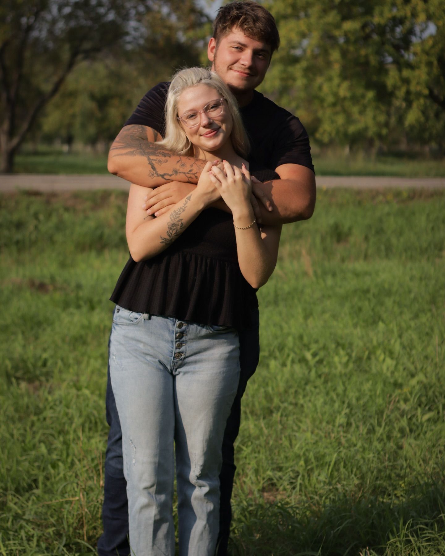Couple embracing in casual outfits against green summer field background.