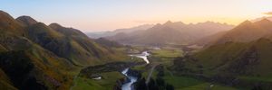 Aerial panoramic view of a lush green mountain valley with a winding river at golden sunset.
