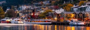 Queenstown waterfront at dusk with glowing lights reflecting on calm harbor waters and boats moored at a scenic pier.