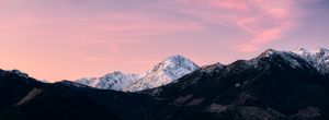 Snow-capped mountain peaks glow under a stunning pink and purple sunset sky in this breathtaking alpine panorama.