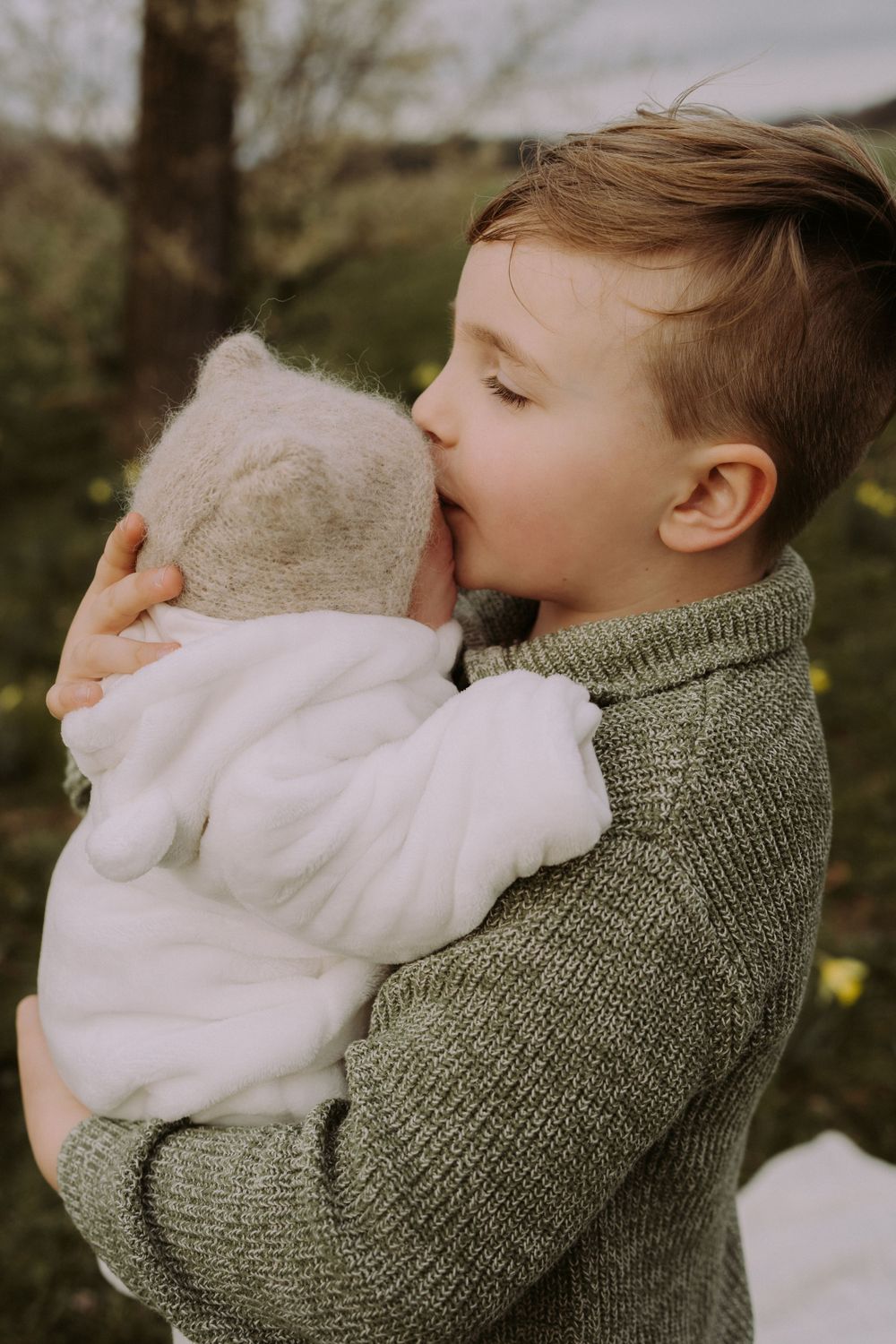 A tender moment captured in a spring garden setting with daffodils and trees in the background.