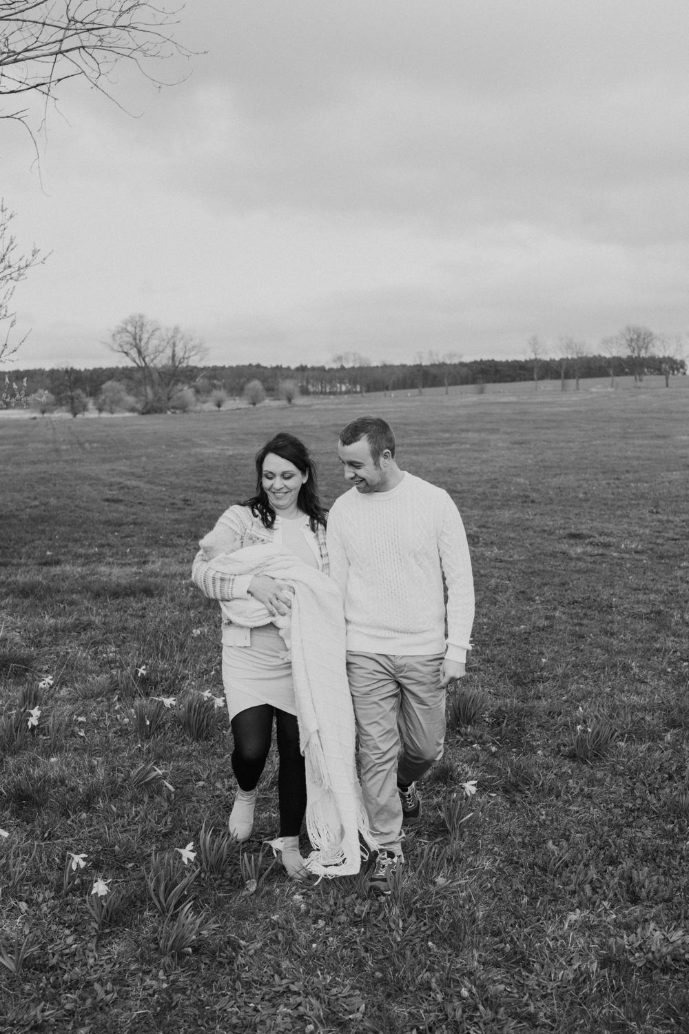 A black and white photograph of a couple walking together in a misty field with their baby.