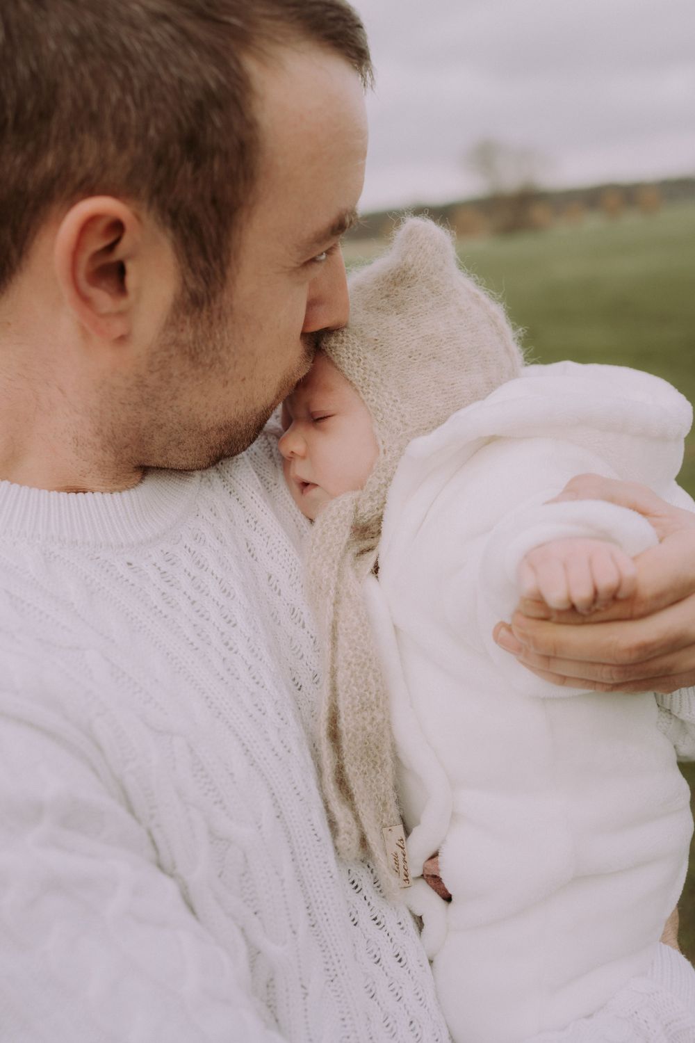 A tender moment between a parent and baby bundled in white winter clothing outdoors.