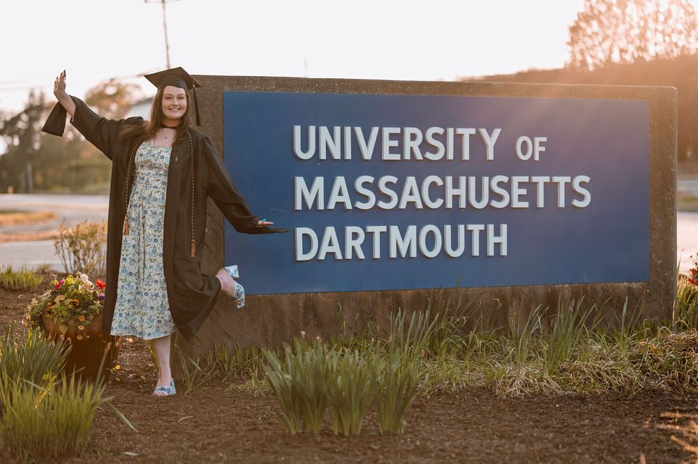 Two graduates in caps and gowns joyfully celebrate their achievement at the University of Massachusetts Dartmouth campus.