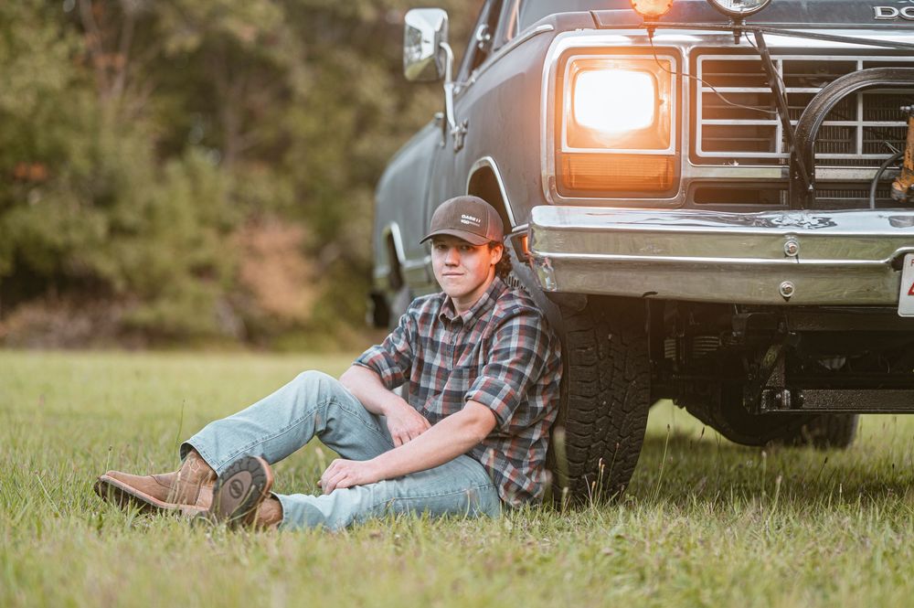 A person in a blue shirt lies in the grass next to a black pickup truck on a sunny day.