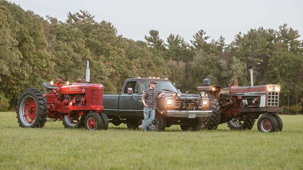 A panoramic view of vintage tractors and farm equipment lined up in a green field during a rural exhibition.