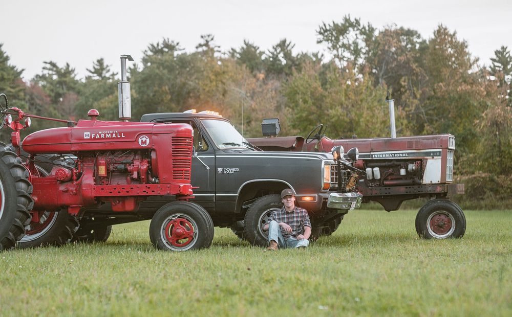 A row of vintage red farm tractors displayed on grass with trees in the background at an outdoor equipment show.