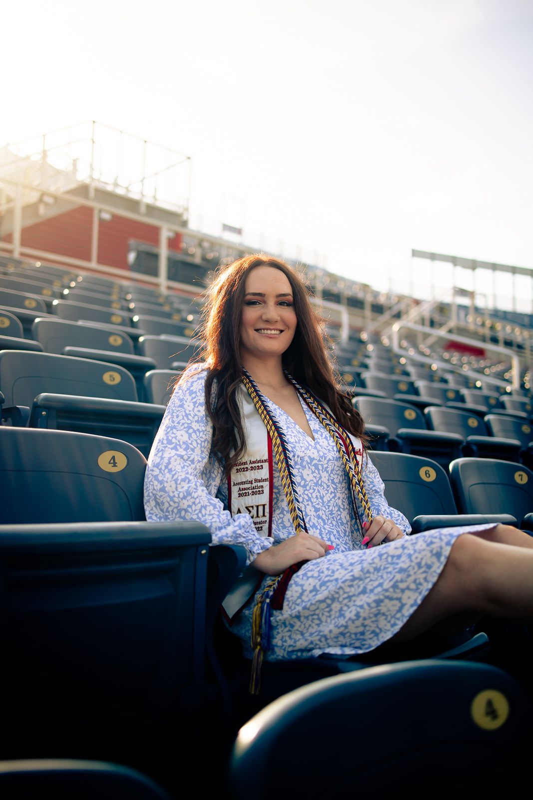 Smiling graduate seated in stadium rows, Fort Lauderdale graduation photo by Mannyportraits for FAU and South Florida universities.
