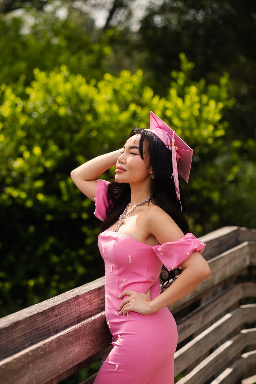 Graduate in pink gown adjusting cap, South Florida graduation portrait by Mannyportraits, perfect for FIU and UM students.