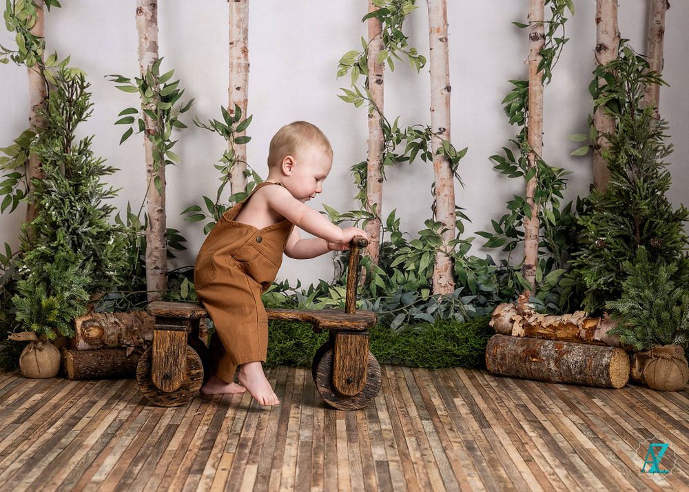 Small child in brown overalls explores rustic woodland scene with wooden bench.