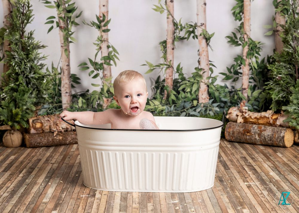 Child plays in white metal tub against rustic woodland backdrop with birch trees.