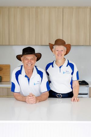 Two people wearing matching uniforms and cowboy hats smiling in kitchen setting.