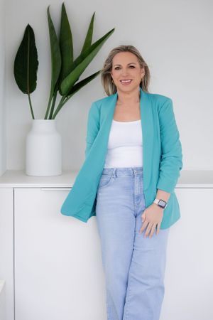 Modern business look with turquoise blazer and jeans against white wall with plants.