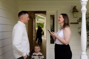 Real estate agent showing home to man and child on front porch of house.
