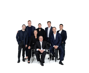 A group of people dressed in dark formal attire pose together on a white background in a business setting.