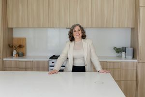 Professional standing confidently at white kitchen counter with modern wood cabinetry and minimalist design.