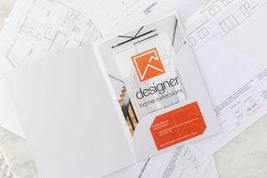 Orange and white designer business card on architectural blueprints with scissors and pencils.