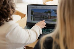 People looking at architectural 3D rendering of a white house design with fence on laptop computer screen.