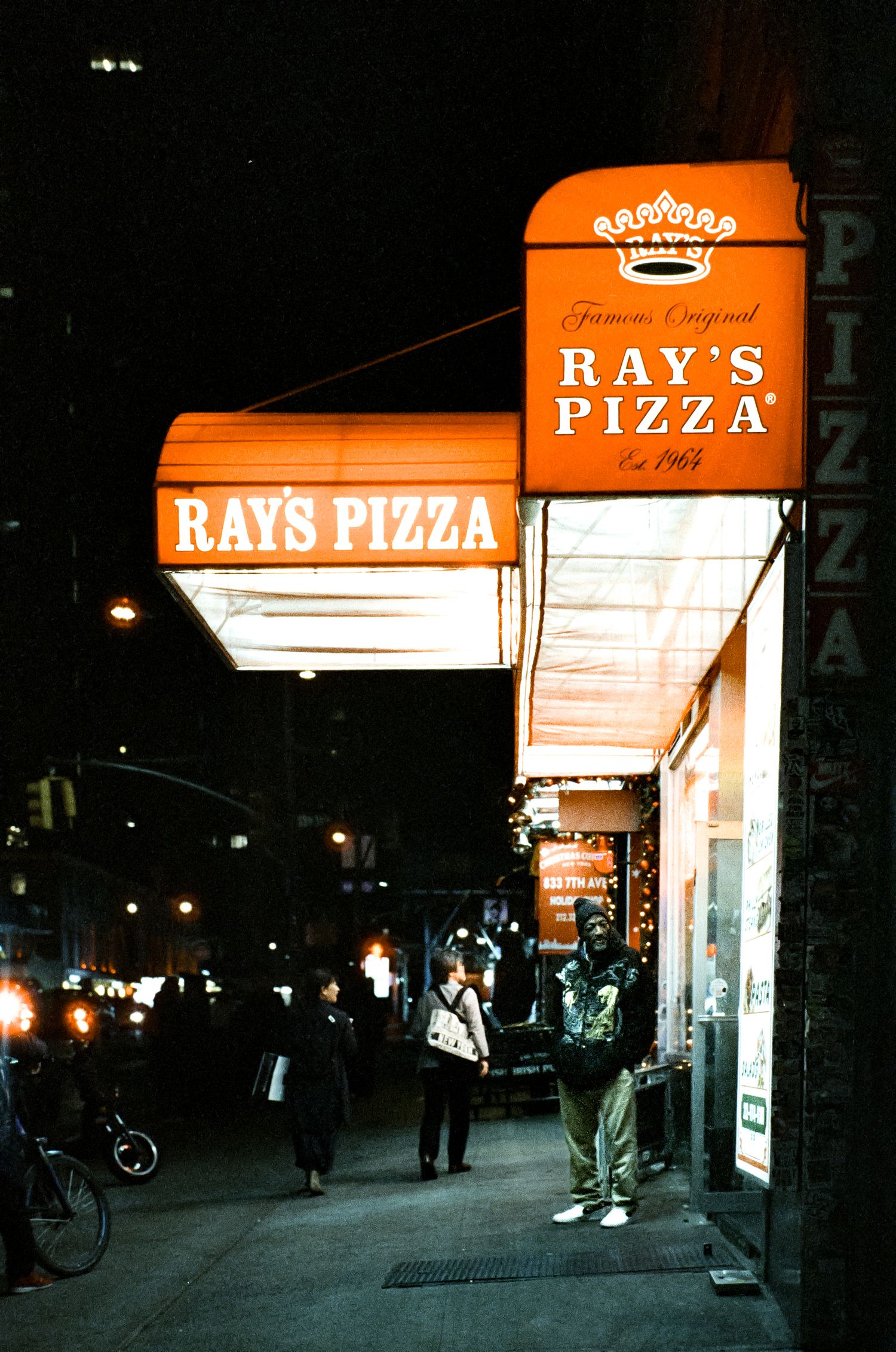 Illuminated Ray's Pizza storefront sign and entrance at night in New York City.