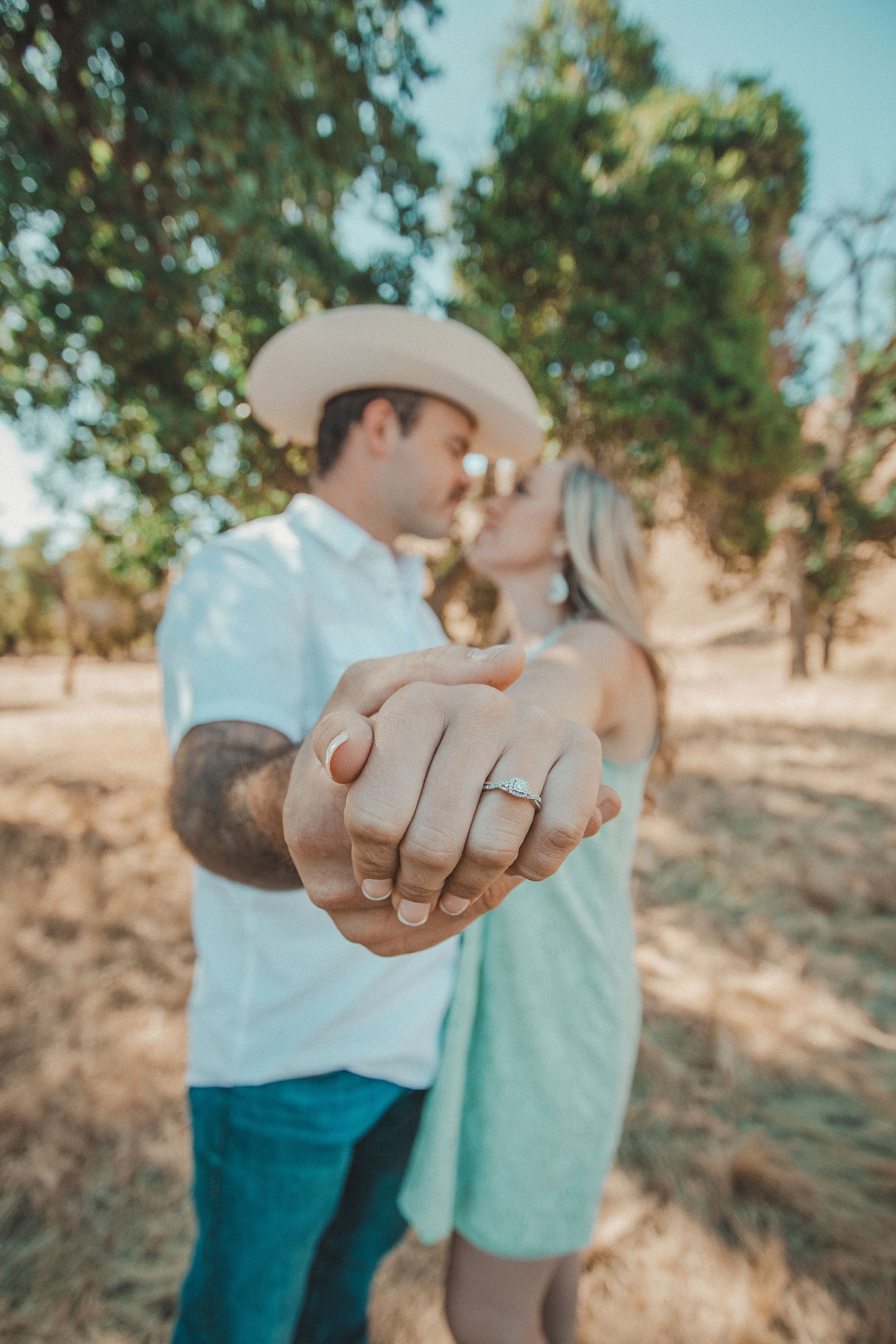 Closeup of joined hands with an engagement ring in a rustic outdoor setting.