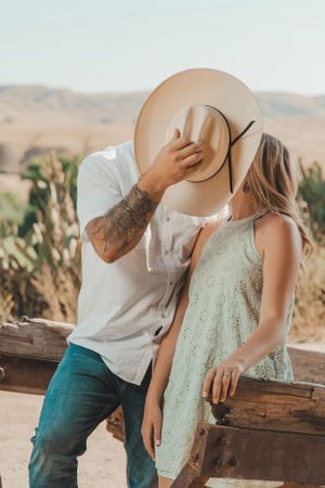 Romantic moment shared on wooden fence with cowboy hat and desert landscape.